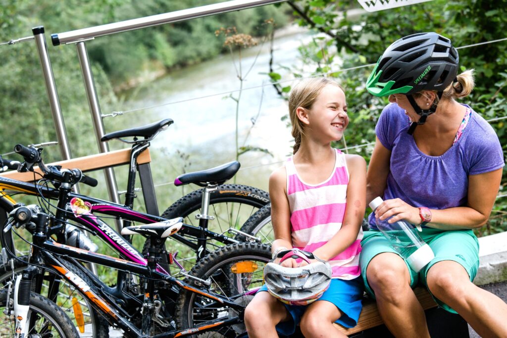 Frau und Kind sitzen neben Fahrrädern auf einer Brücke mit Fluss im Hintergrund
