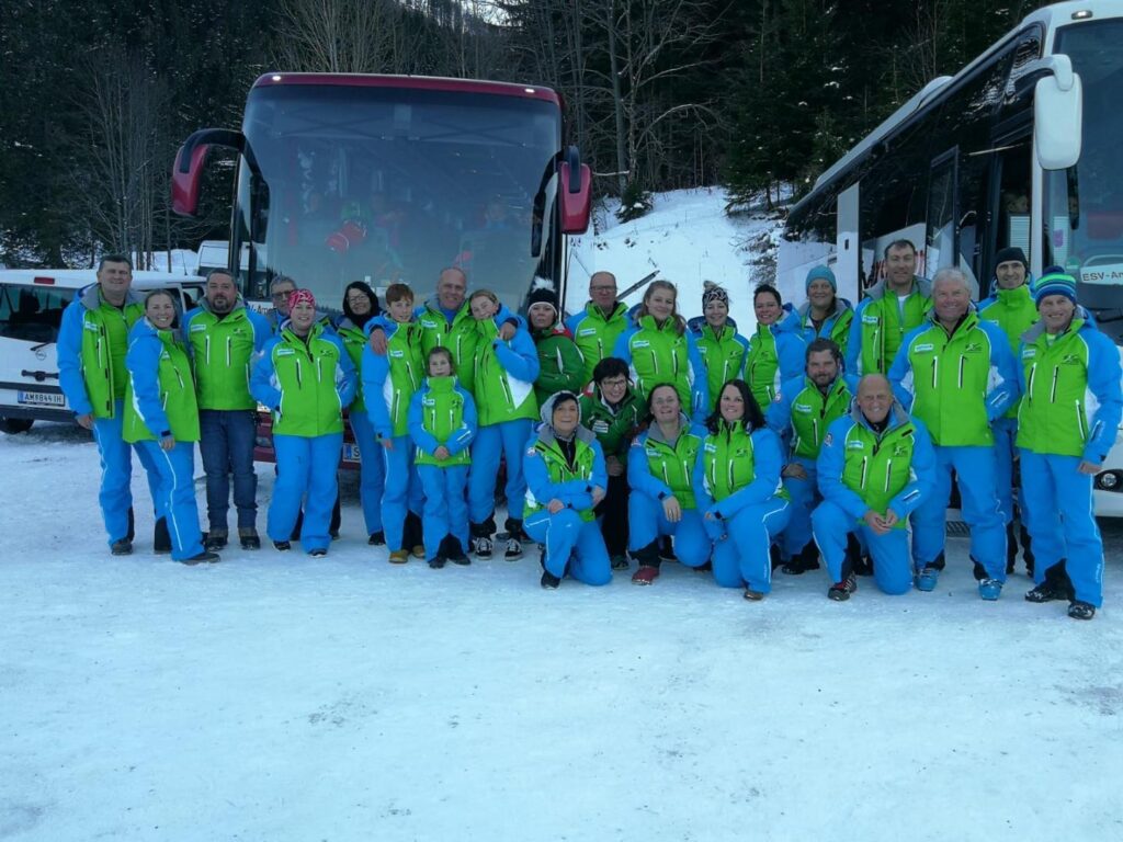 Gruppenfoto von Vereinsmitgliedern im Skioutfit vor Reisebussen im Schnee