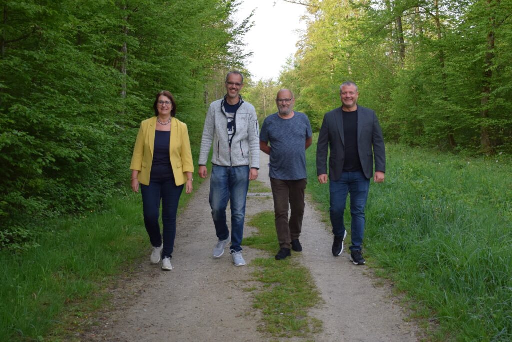 Umweltgemeinderätin Michaela Pfaffeneder, Tourbegleiter und Hobbyentomologen Peter Tomazic und Johann Ortner sowie Vizebürgermeister Dominic Hörlezeder gehen auf einem Waldweg in der Forstheide.